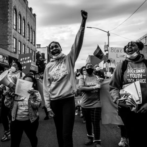 Protesters marching with banners and a megaphone with one person holding a fist in the air
