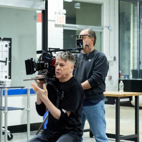 Man sits holding a camera while other look on