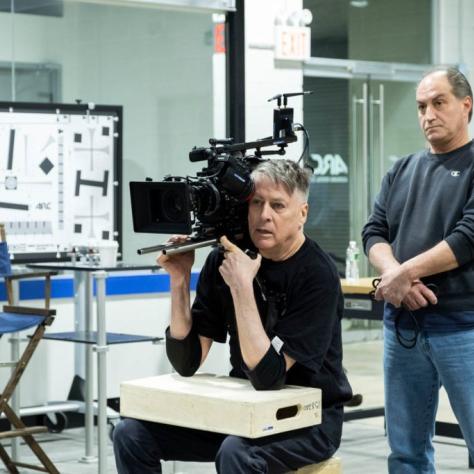 Man sits holding a camera and another behind him watches