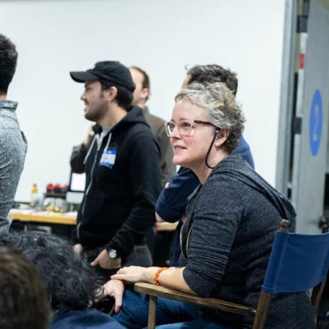 Woman with glasses sits in a chair while others stand