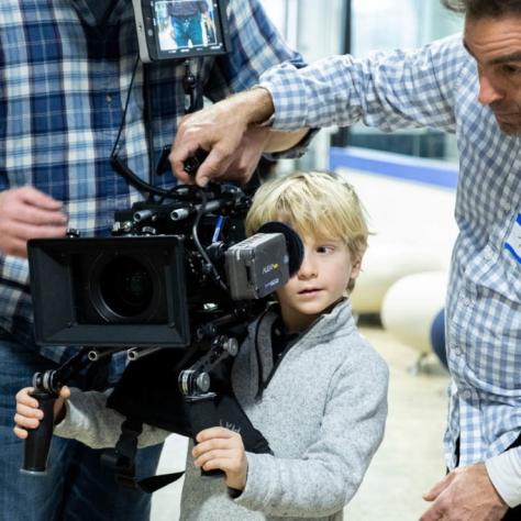 Man holds camera and a child looks through it