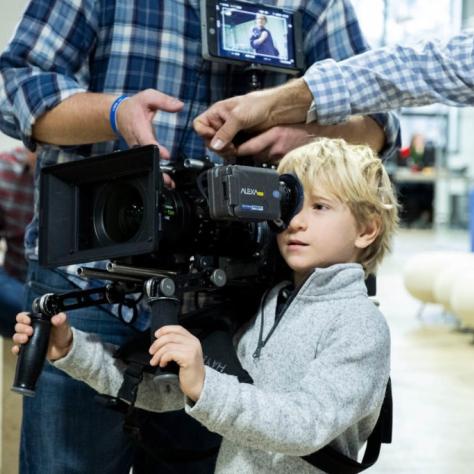 Man holds camera and a child looks through it