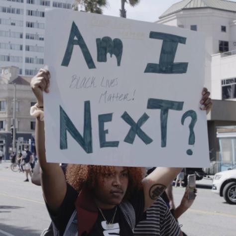Woman holding a sign that reads "Am I Next?"